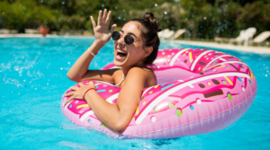 Girl smiling and swimming in a pool with sunglasses on.