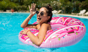 Girl smiling and swimming in a pool with sunglasses on.