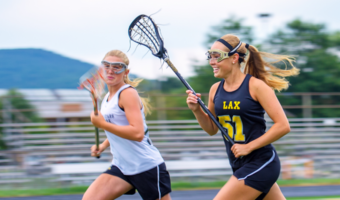 Two girls running and playing lacrosse.