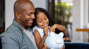Father and daughter smiling and putting money in a piggy bank.