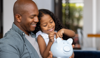 Father and daughter smiling and putting money in a piggy bank.