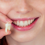 Person smiling and holding a wisdom tooth.