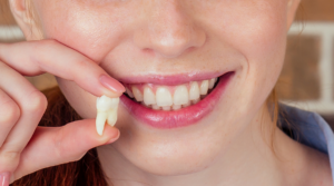 Person smiling and holding a wisdom tooth.