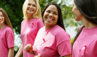 Group of women smiling and wearing pink with breast cancer ribbons.