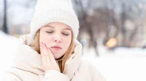 Person standing in the snow, holding their jaw in pain.