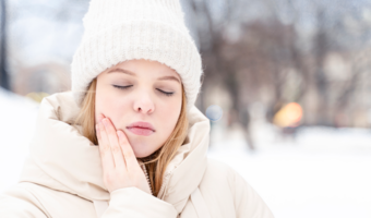 Person standing in the snow, holding their jaw in pain.