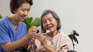 Dental assistant helping older adult brush and floss teeth.