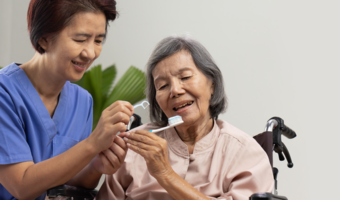 Dental assistant helping older adult brush and floss teeth.