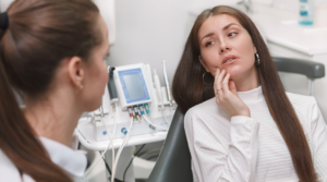Person sitting in a dental chair, holding their jaw in pain.