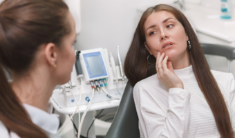 Person sitting in a dental chair, holding their jaw in pain.