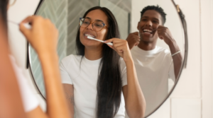 One person brushing their teeth and another flossing in the mirror together.
