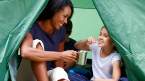 Child brushing their teeth in a tent with her mother.