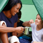 Child brushing their teeth in a tent with her mother.