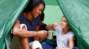 Child brushing their teeth in a tent with her mother.