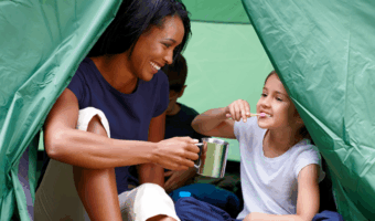 Child brushing their teeth in a tent with her mother.